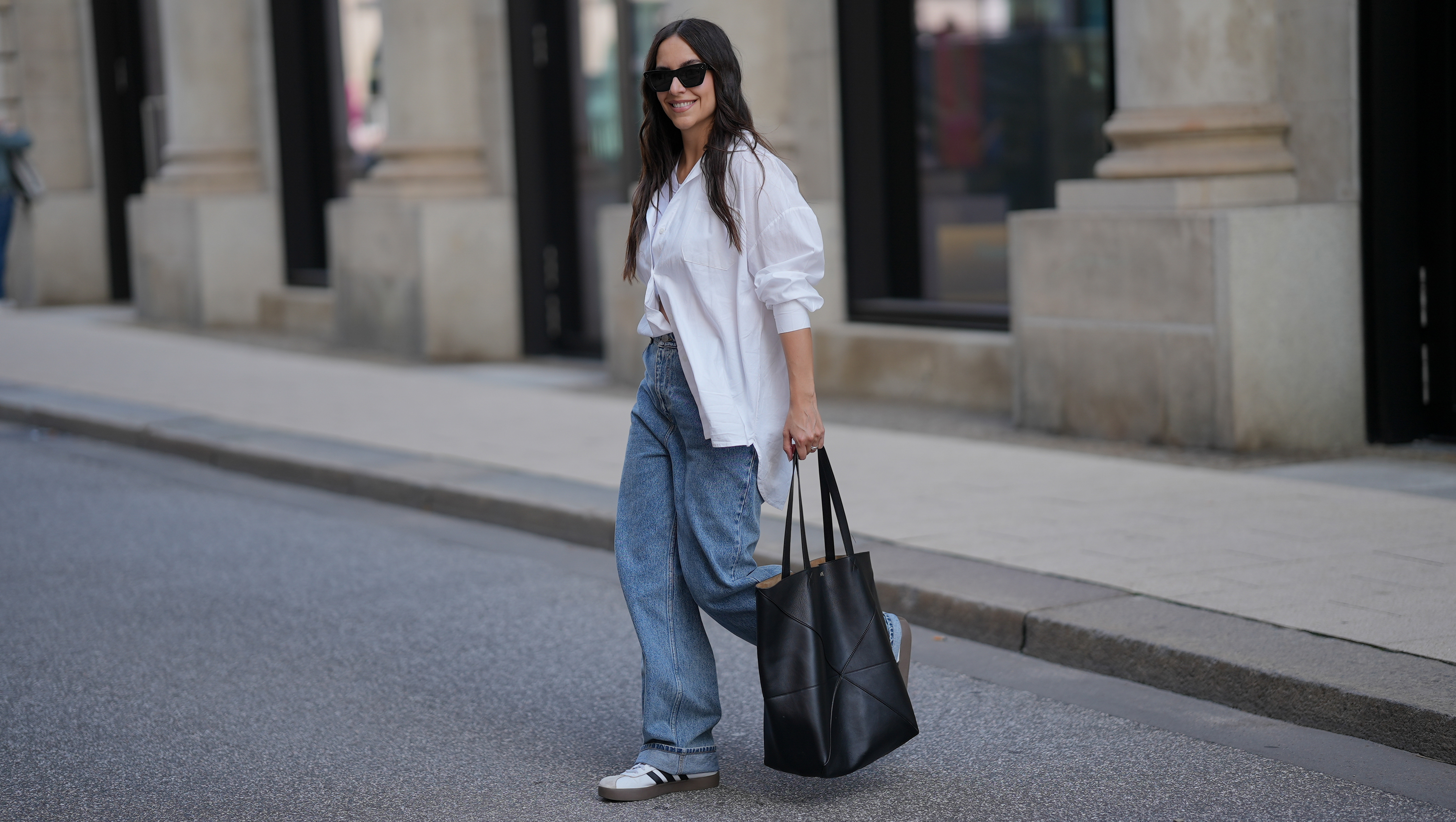 HAMBURG, GERMANY - SEPTEMBER 19: Jessica Schöne is seen wearing an oversized crisp white button-up shirt with a relaxed fit and rolled up sleeves, worn partially tucked into the front of her jeans; a white crew-neck T-shirt layered underneath; light blue straight-leg jeans with a loose, slightly slouchy silhouette; white low-top Adidas VL Court 3.0 sneakers with contrasting brown soles and black side stripes from Adidas; a large folded black leather Puzzle Tote shopper bag from Loewe; stacked gold and silver rings on her fingers; black acetate cat eye sunglasses; her long dark hair is worn down in soft natural waves on September 19, 2025 in Hamburg, Germany. (Photo by Moritz Scholz/Getty Images)