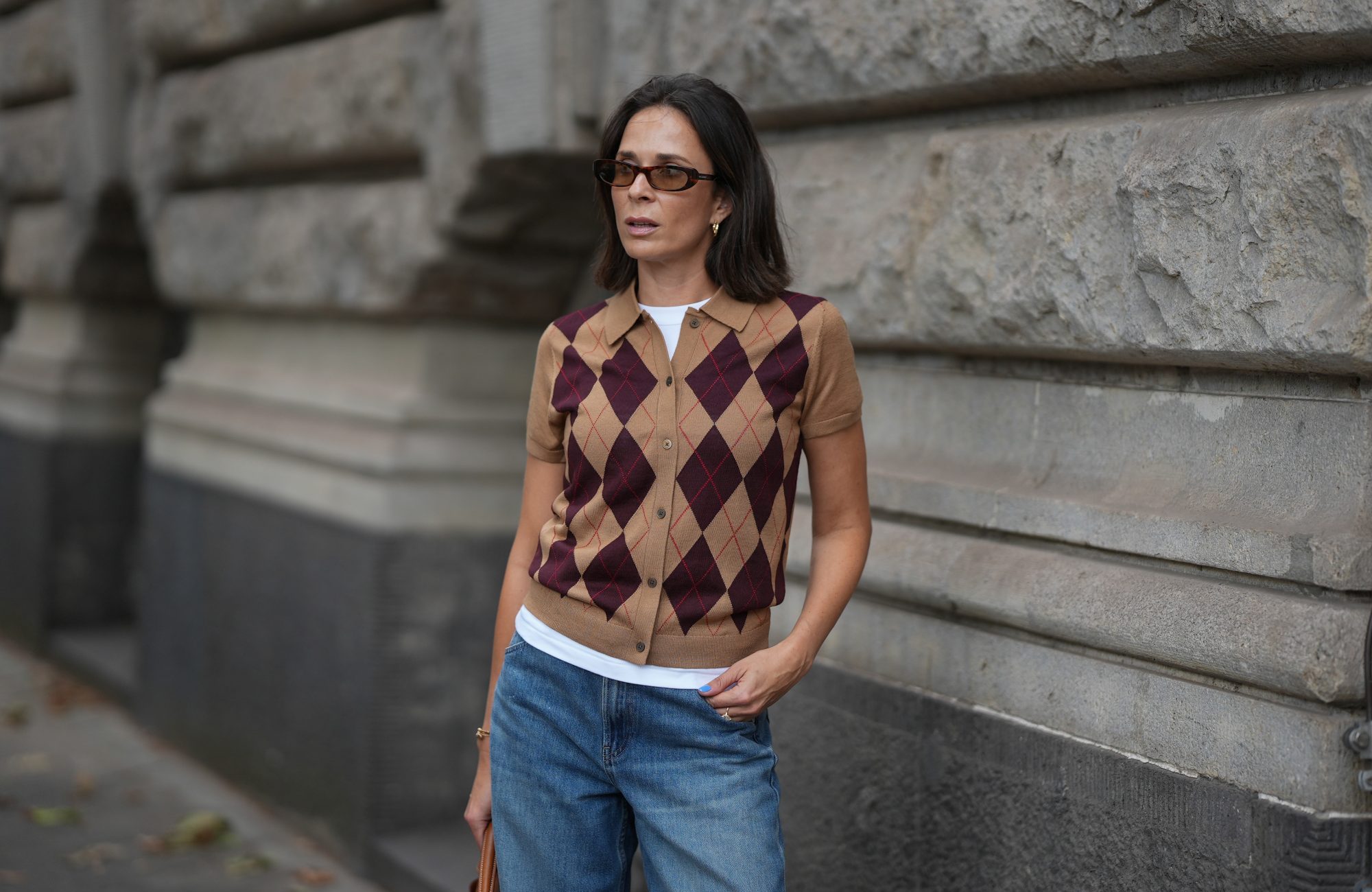 DUESSELDORF, GERMANY - AUGUST 31: Patricia Wirschke is seen wearing brown argyle short sleeve knit top from Uniqlo over a white T shirt from Uniqlo; blue wide leg jeans from Uniqlo; rectangular acetate sunglasses with dark tinted lenses from YSL; dark brown hair worn loose with a center part on August 31, 2026 in Duesseldorf, Germany. (Photo by Moritz Scholz/Getty Images)
